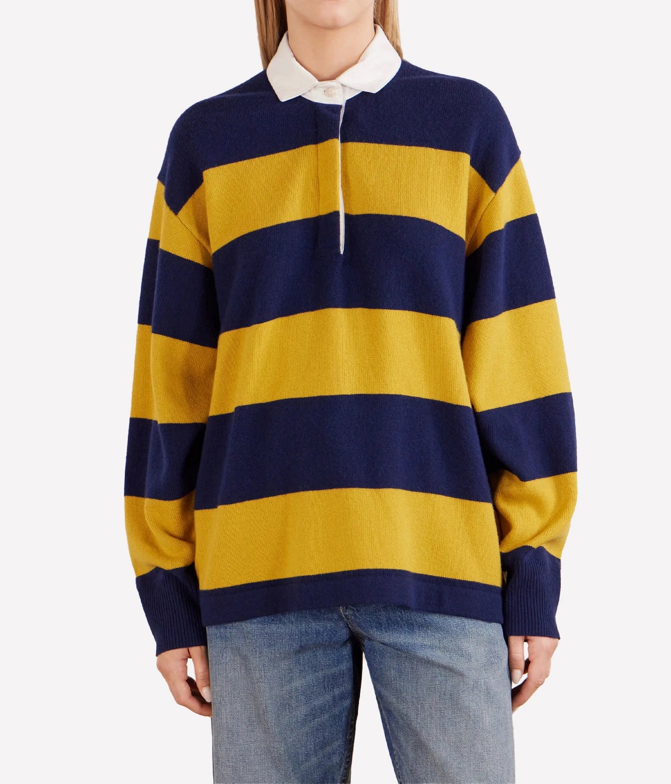 A model wearing a navy blue and mustard yellow striped knit rugby sweater with a white collar, paired with blue jeans, against a light gray background.