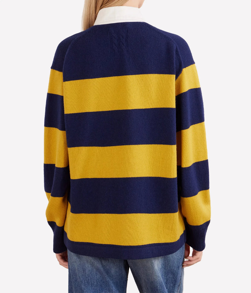 A person shown from the back wearing a knit sweater with wide horizontal navy and mustard yellow stripes, paired with blue jeans against a light gray studio background.