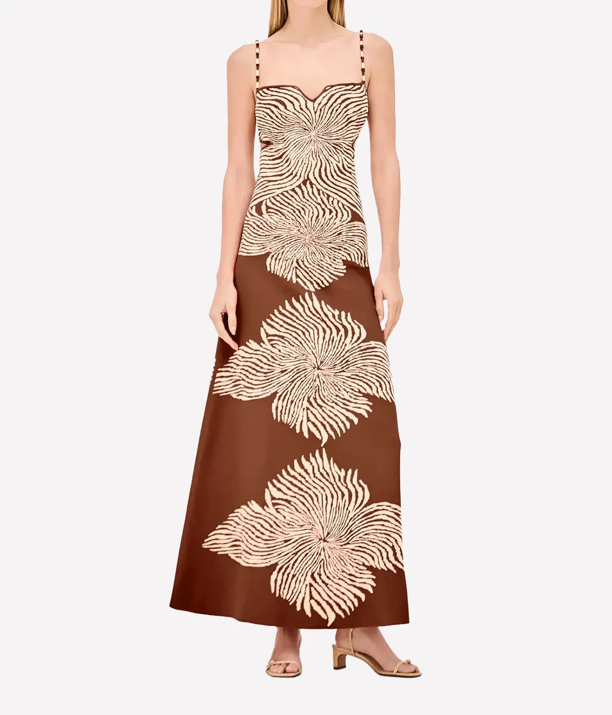 Front view of a model wearing the Alexis Rayana Dress In Brown Blossom with nude strappy sandals, showing the thin straps and close-fitting silhouette falling to the ankle