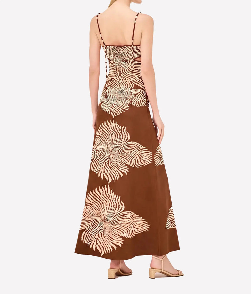 Back view of a model wearing the Alexis Rayana Dress In Brown Blossom, showing the thin straps, fitted back and large cream floral motifs down the skirt