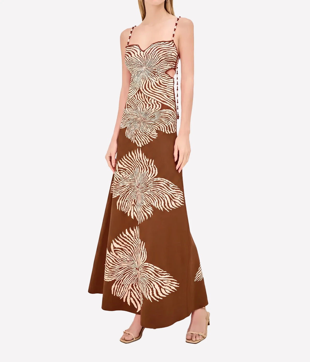 Three-quarter side view of a model wearing the Alexis Rayana Dress In Brown Blossom with nude strappy sandals, showing the streamlined fit through the body and skirt