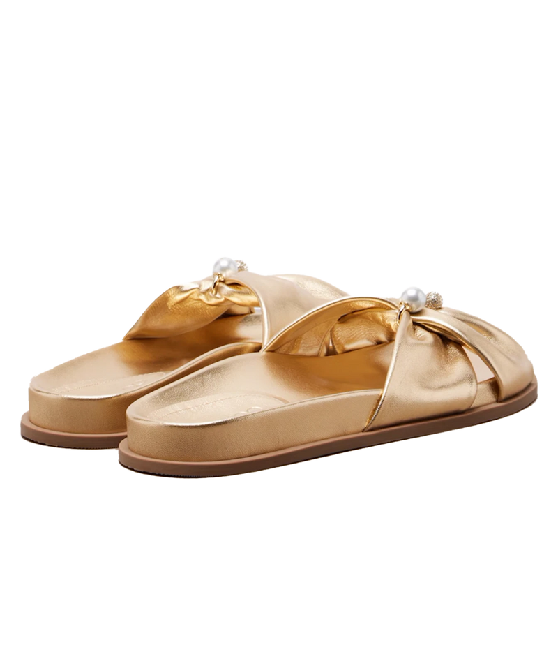 A pair of metallic gold slide sandals with wide crisscross straps, decorative fabric bows, and small pearl accents on the straps, shown against a plain white background.