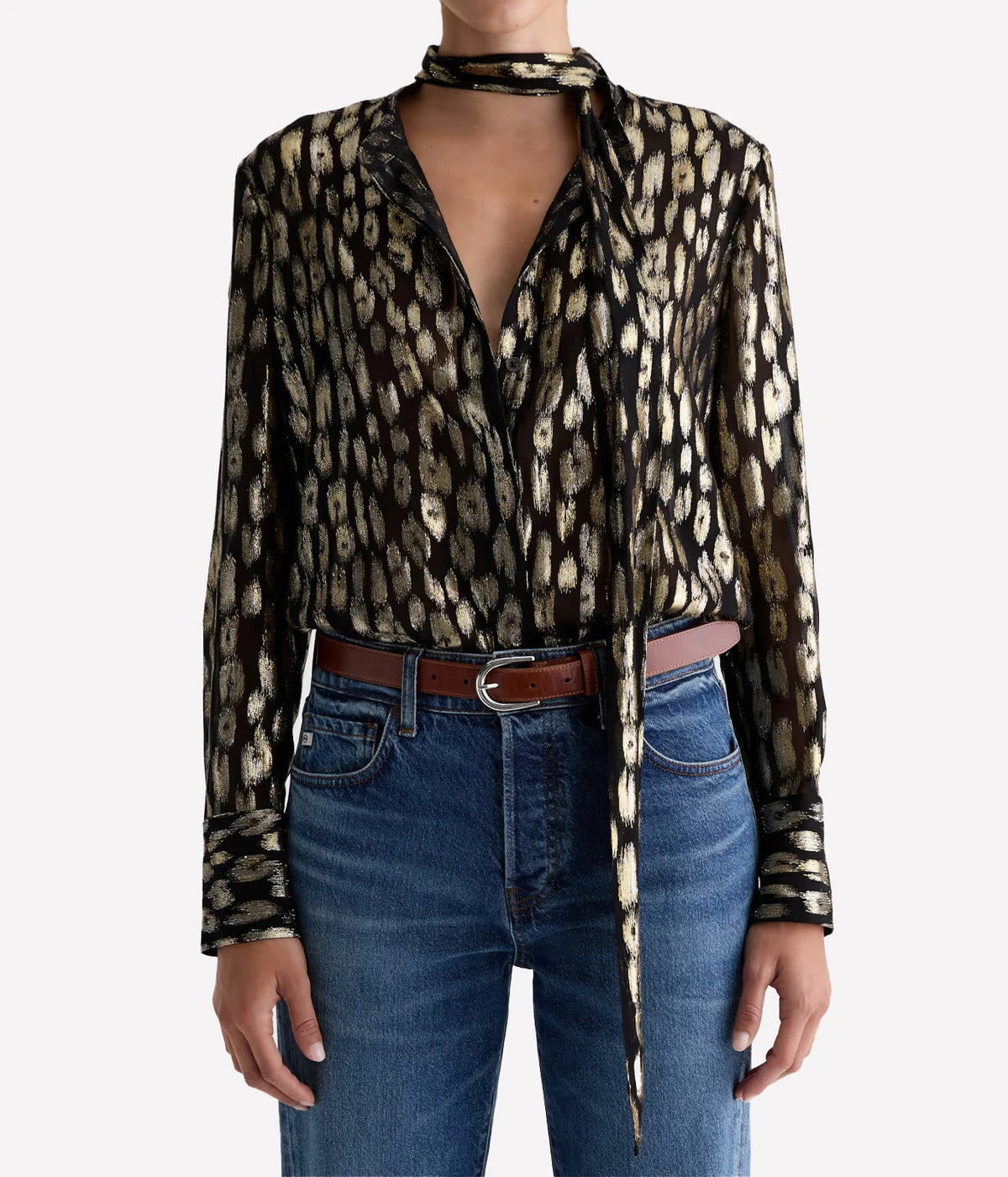 Model wearing the AG Lora Tie Neck Shirt in Leopard Lounge tucked into mid-blue jeans with a brown leather belt, the tie neck knotted loosely with long ends hanging down the front