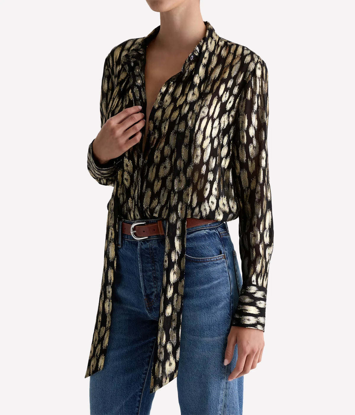 Three-quarter view of a model adjusting the tie of the AG Lora Tie Neck Shirt in Leopard Lounge, worn tucked into blue jeans with a brown leather belt