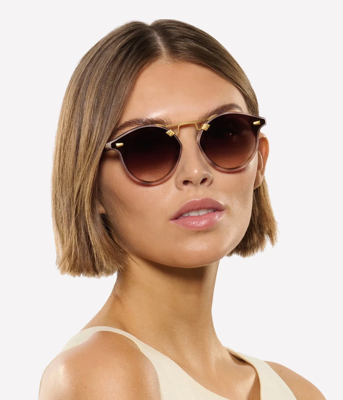 Three-quarter view of a model with a short bob wearing the KREWE STL Nylon Sunglasses in 18K Matte Blush Tortoise with a cream top