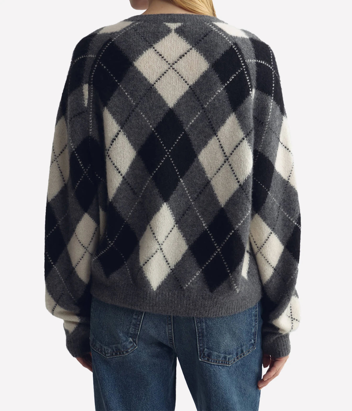 A person shown from the back wearing a fuzzy knit sweater with a large argyle pattern in dark gray, black, and off-white, paired with blue jeans against a light gray studio background.