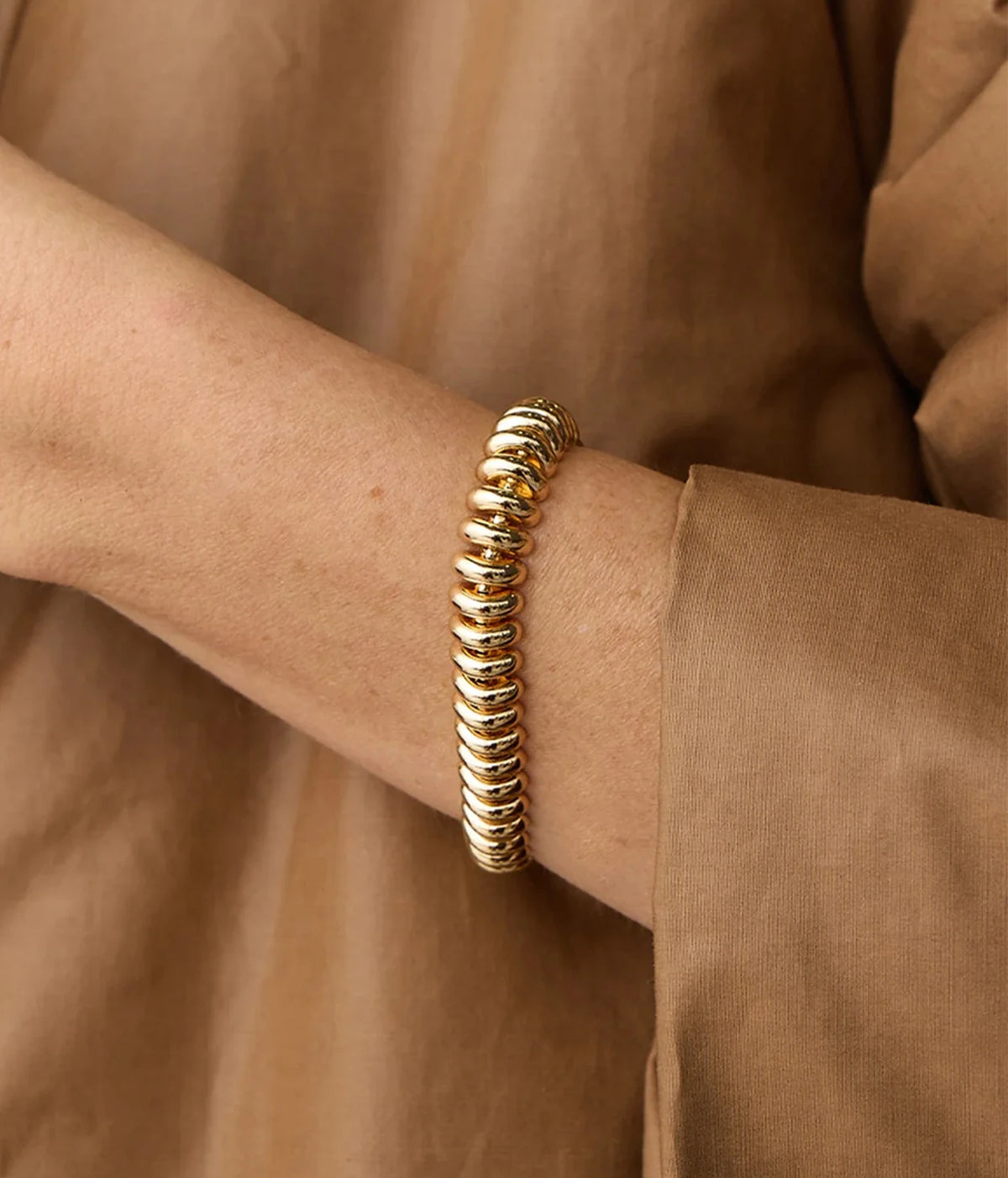 Model wearing the Jenny Bird Sofia Bracelet in Gold on her wrist with a camel long-sleeve top