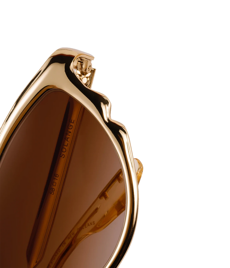 Close-up of the KREWE Solange Sunglasses in 18K Chroma Champagne, showing the convex mirrored gold finish at the hinge