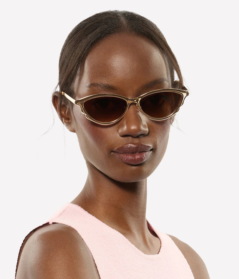 Model with her hair pulled back wearing the KREWE Solange Sunglasses in 18K Chroma Champagne with a pale pink sleeveless top