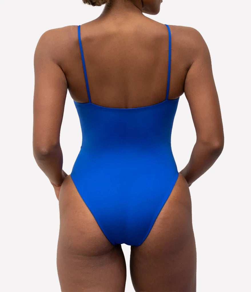 The model wears the Sunday Suit in First Place, a flattering bright royal blue swimsuit. This one piece is perfect for the pool, the beach or the city, with a V neckline, thin straps and medium coverage, as well as a high cut legline. 