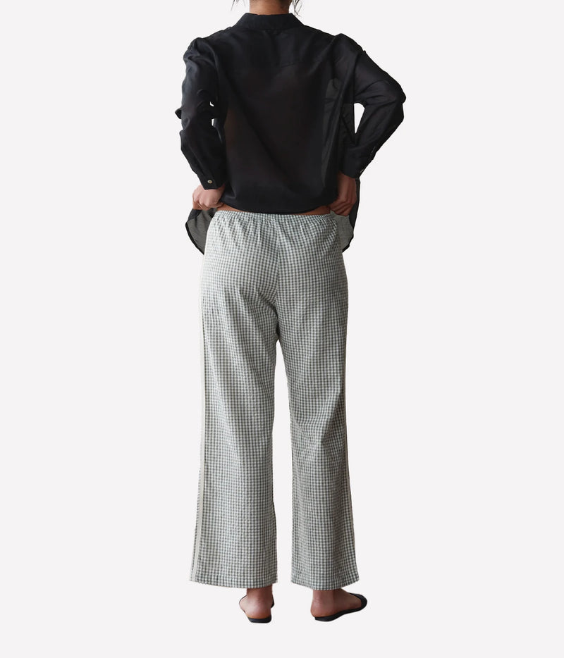 A model shown from the back wearing a black long-sleeve blouse and light gray and black checkered wide-leg trousers, set against a plain light gray background.