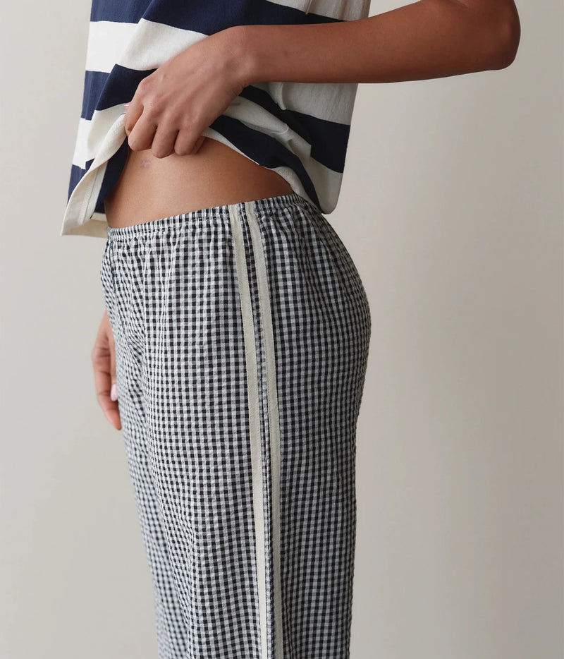 Model wearing navy gingham check pants with a striped tank top, side profile view showing the waistband and contrast stripe.