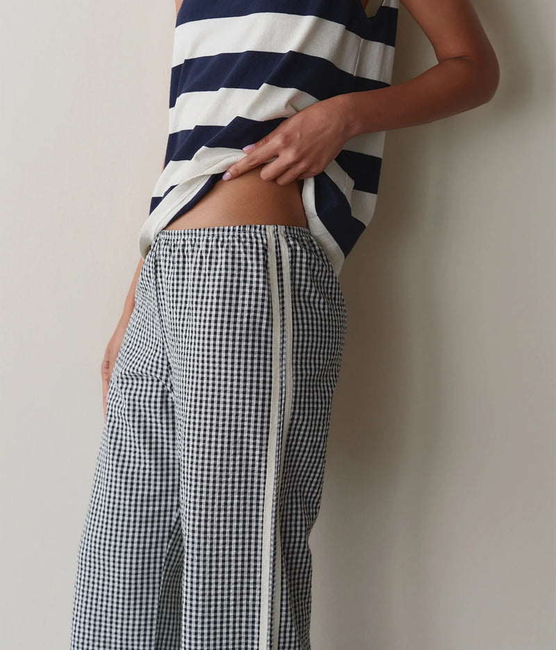 Model wearing navy gingham check pants, side view against a wall showing the waistband and side stripe detail.
