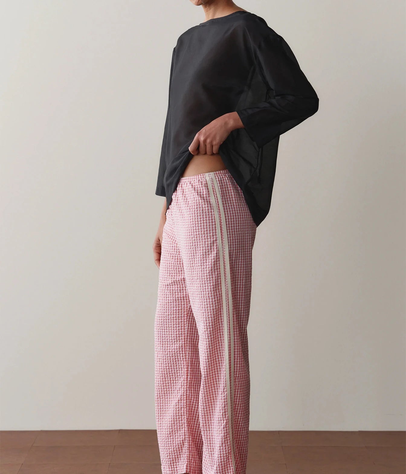 Model wearing pink gingham check pants with a black long-sleeve top, side profile view showing the straight-leg silhouette.