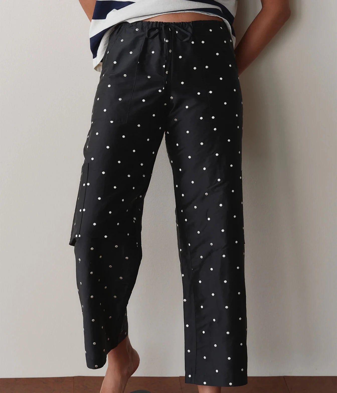 Model wearing black polka dot cargo pants, side view leaning against a wall to show the side cargo pocket and leg silhouette.