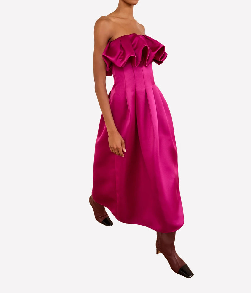 A model wearing a bright magenta strapless maxi dress with a ruffled off-the-shoulder neckline, a structured waist, and a voluminous skirt, Ulla Johnson Cosima Strapless Satin Dress in Orchid