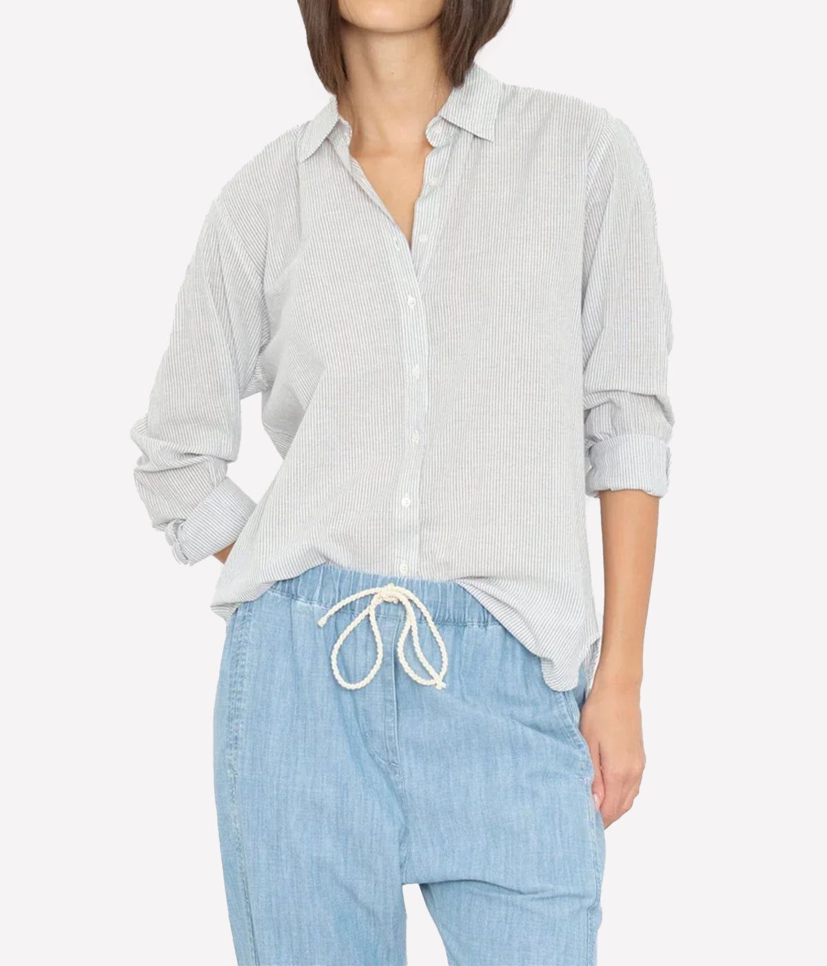 Model wearing the Xirena Beau Shirt in Windward Stripe loosely tucked into light chambray drawstring pants with sleeves rolled, showing the fine vertical stripe and point collar
