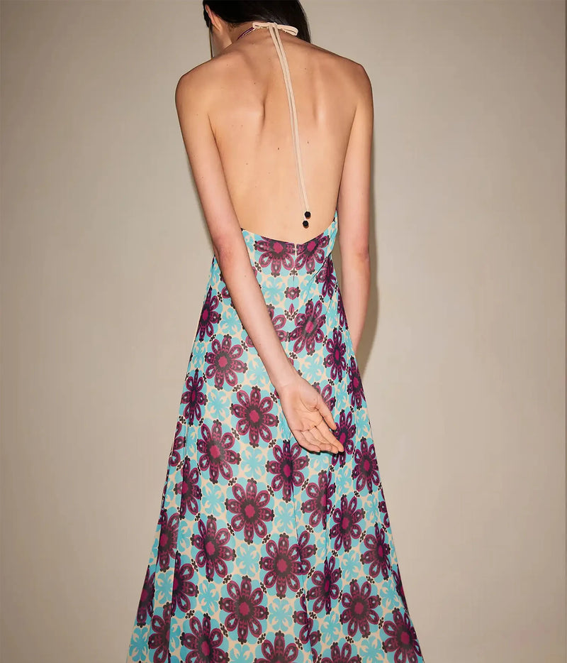 Back view of a model wearing the Alexis Azurea Dress In Jardin Sable, showing the halter neck tie and open low back above the flowing printed skirt