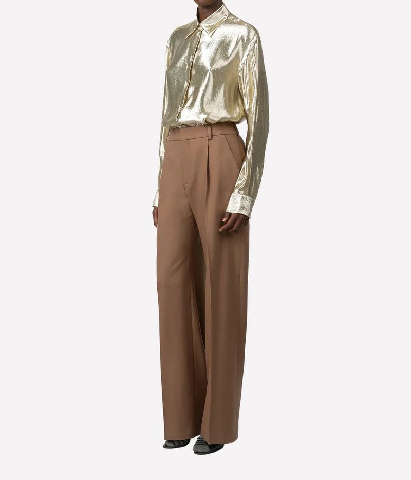 A model wearing a metallic gold long-sleeve button-up shirt and high-waisted, wide-leg brown trousers, photographed against a solid light gray background.
