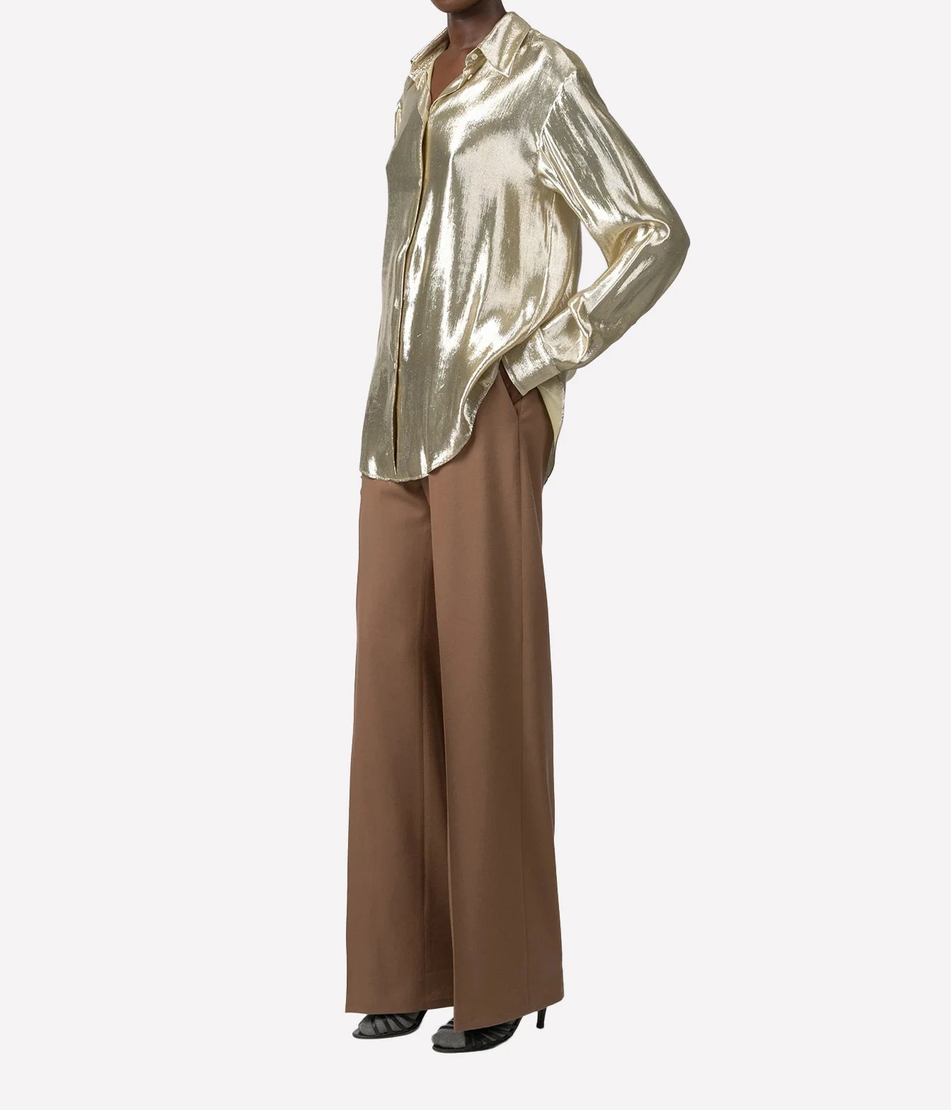 A model wearing a shiny metallic gold button-up shirt and wide-leg brown trousers, shown from the neck down against a light gray background.