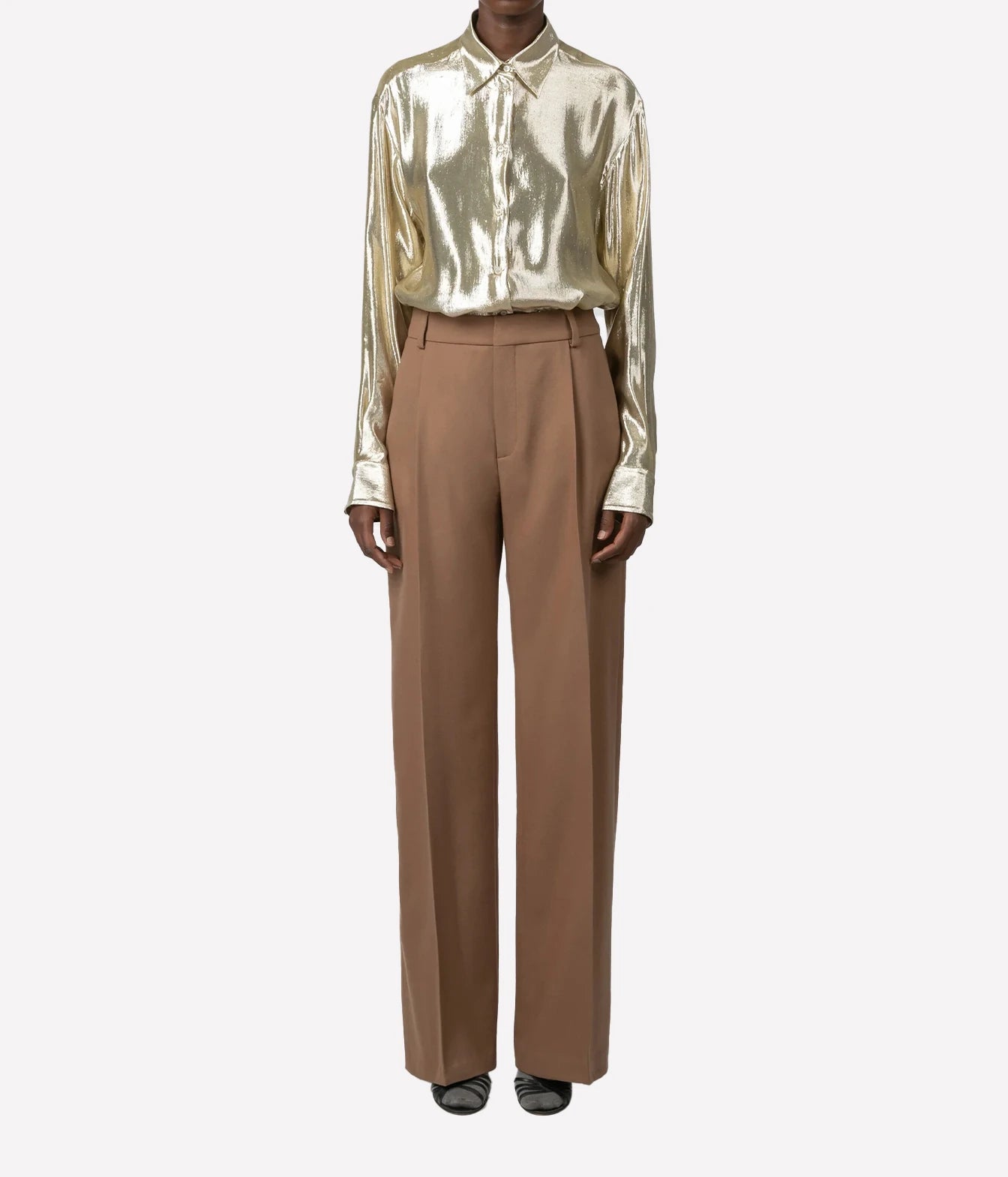 A model wearing a metallic gold satin long-sleeve button-up shirt and brown wide-leg trousers, standing against a light gray background.