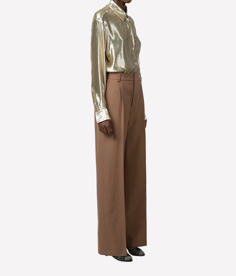 A model wearing a metallic gold long-sleeve mock-neck shirt and high-waisted, wide-leg brown trousers, shown from the neck down against a plain light gray background.