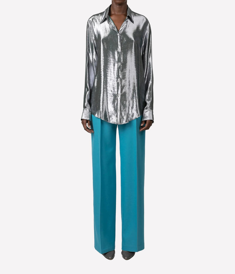 A model wearing a metallic silver long-sleeve button-up shirt and bright teal wide-leg trousers, shown against a plain light gray background.
