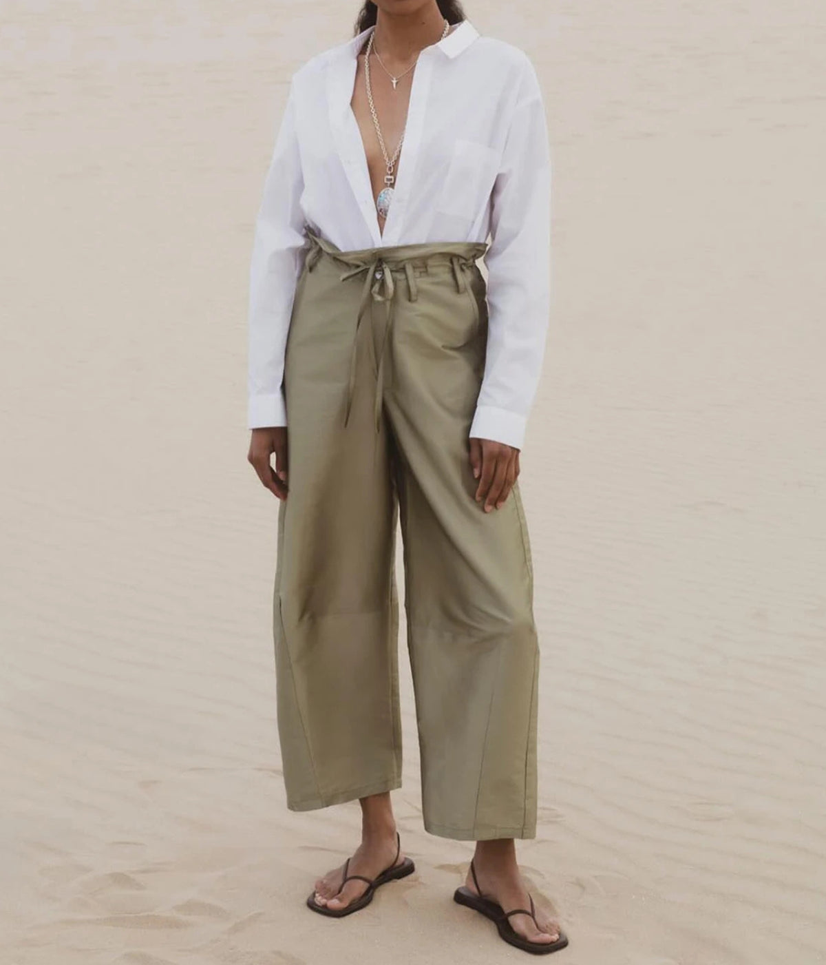 Model wearing sage green wide-leg pants with a tie waist, styled with a white button-down shirt and flat sandals.