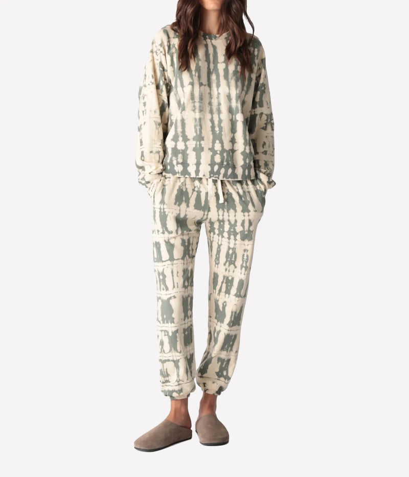 Full-length front view of a model wearing the Electric Rose Classic Horizon Jogger in Moss Ivory with a matching cropped tie-dye sweatshirt, hands in pockets and taupe suede clogs