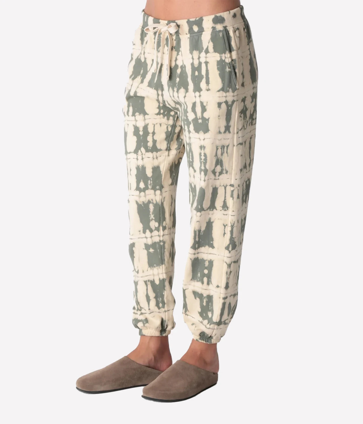 Three-quarter side view of a model wearing the Electric Rose Classic Horizon Jogger in Moss Ivory, showing the relaxed tapered leg and side pocket, with taupe suede clogs