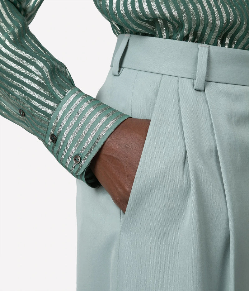Close-up of a person wearing high-waisted light sage green pleated trousers with a matching waistband, paired with a green and silver striped long-sleeve shirt.