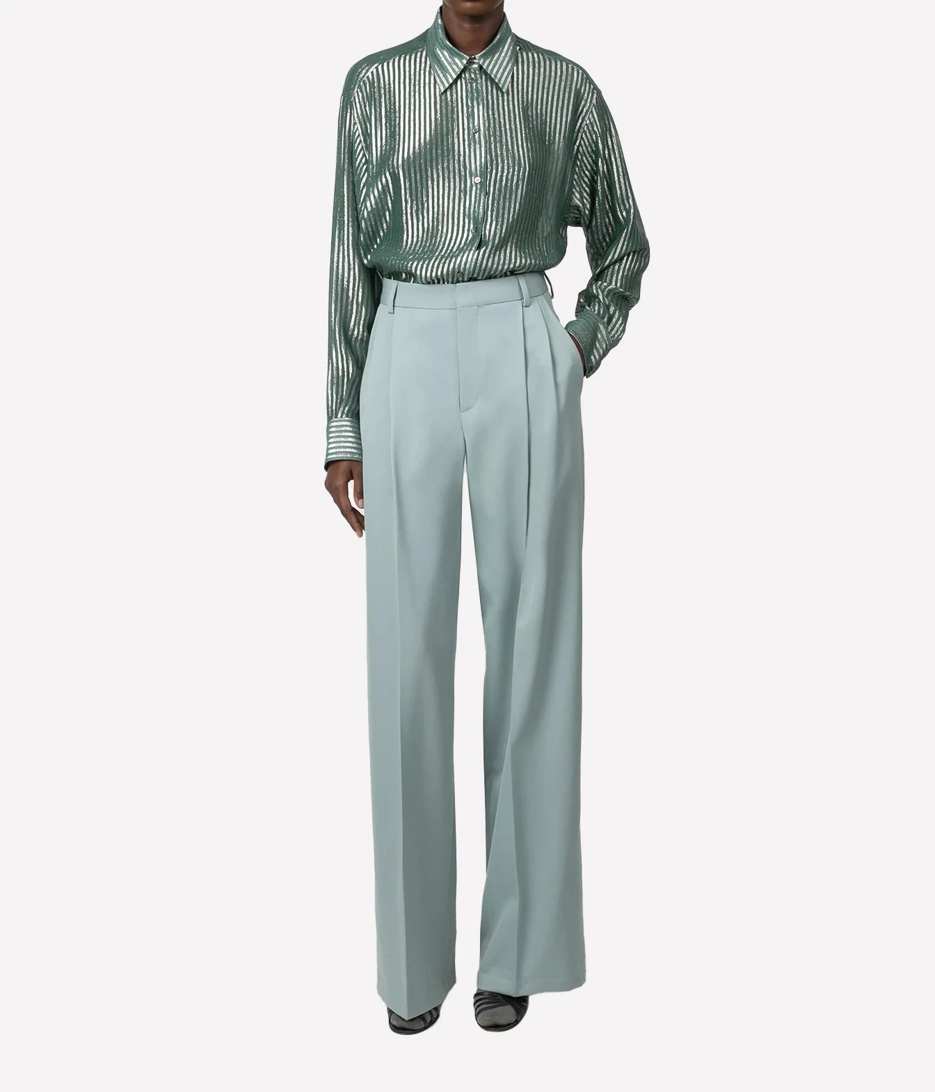 A model wearing a green and white vertically striped long-sleeve button-up shirt tucked into high-waisted, wide-leg light blue trousers, shown against a plain light gray background.