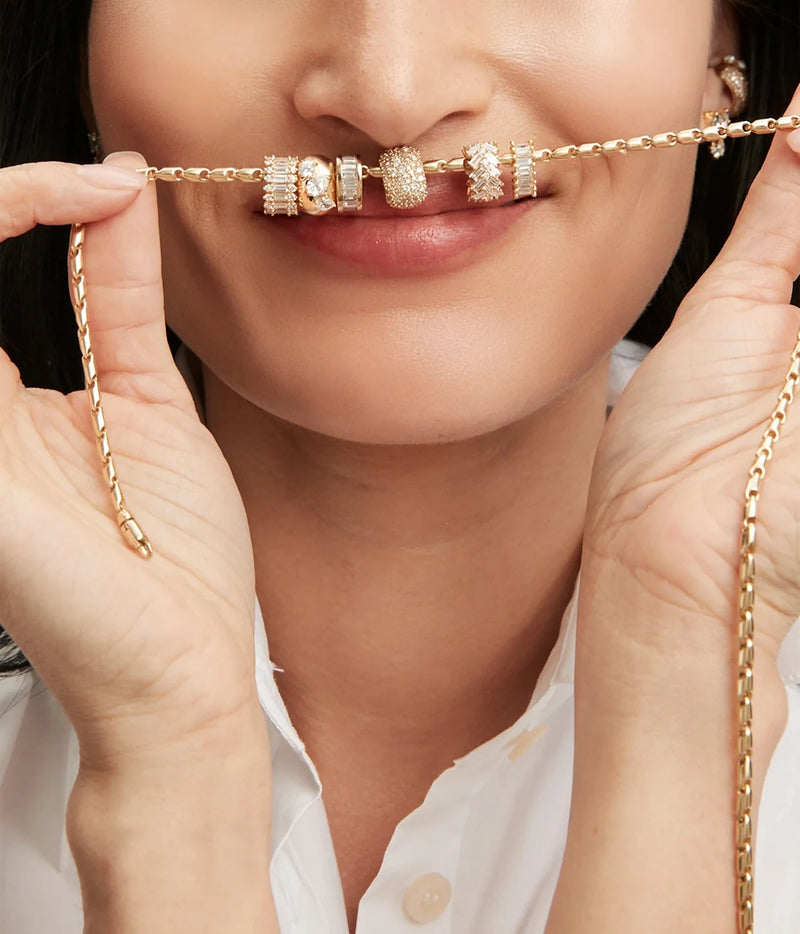Smiling model holding up a gold chain strung with the Adina Reyter Diamond Full Stack Baguette Big Bead in 14K Yellow Gold