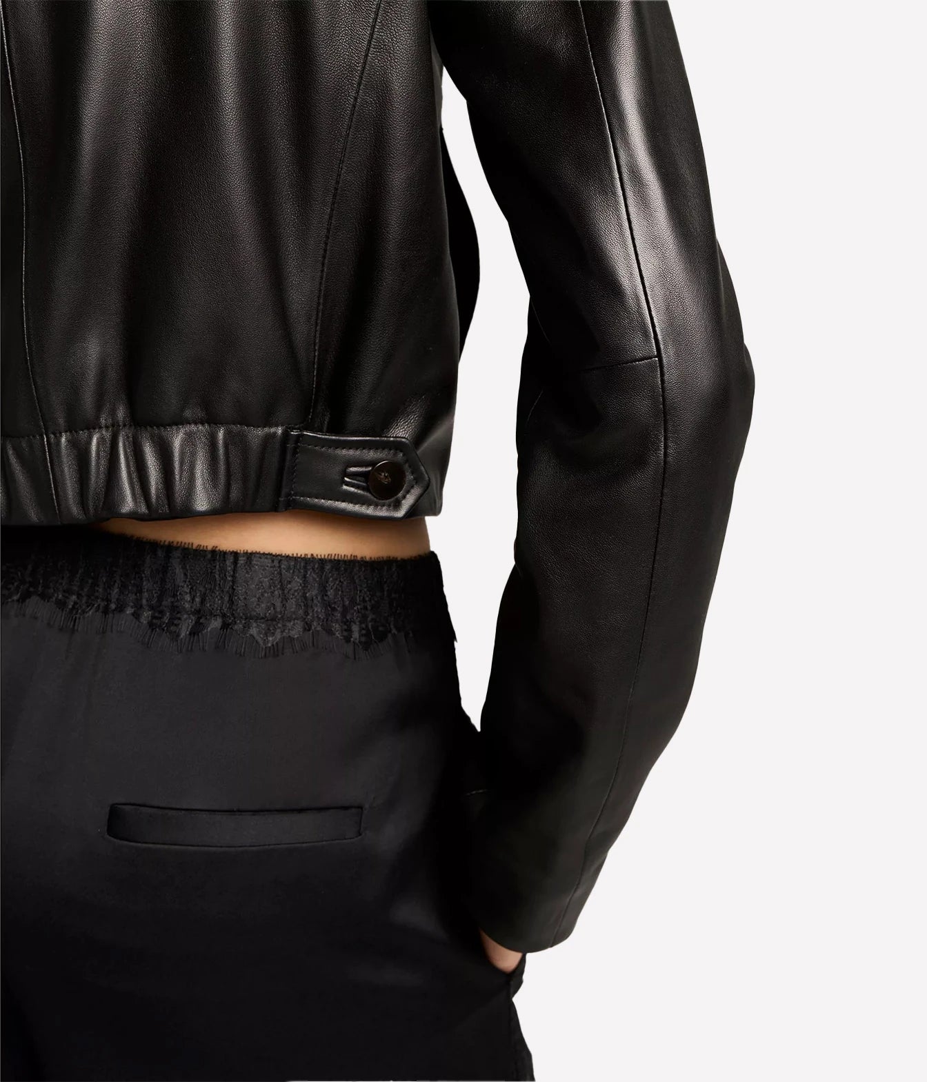 Close-up of a person wearing a black leather cropped jacket with a button tab detail