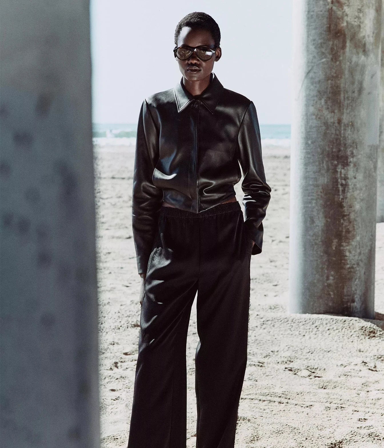 A model wearing a black leather long-sleeve collared shirt and matching black wide-leg trousers