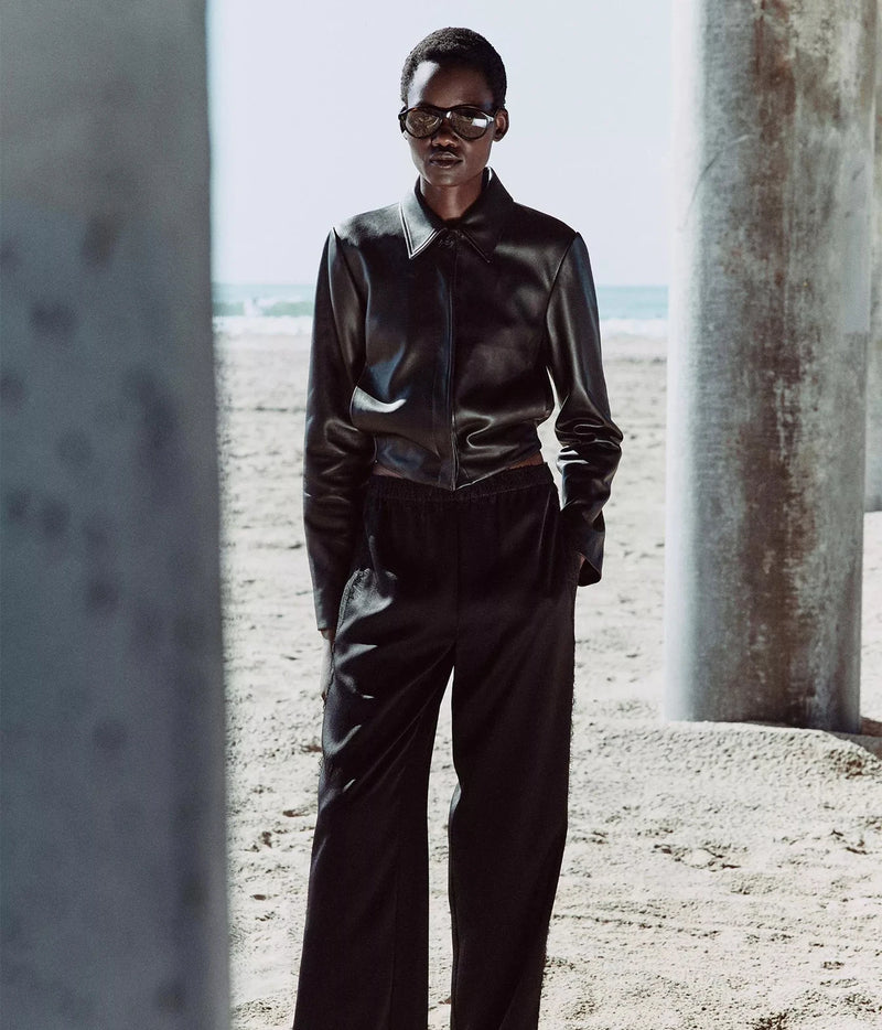 A model wearing a black leather long-sleeve collared shirt and matching black wide-leg trousers