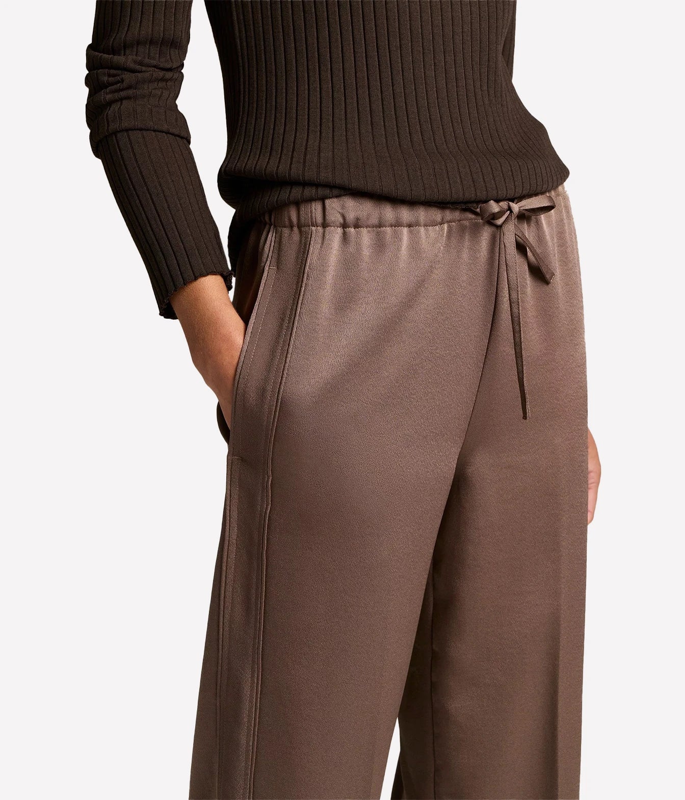 A close-up of a person wearing wide-leg taupe-brown drawstring sweatpants