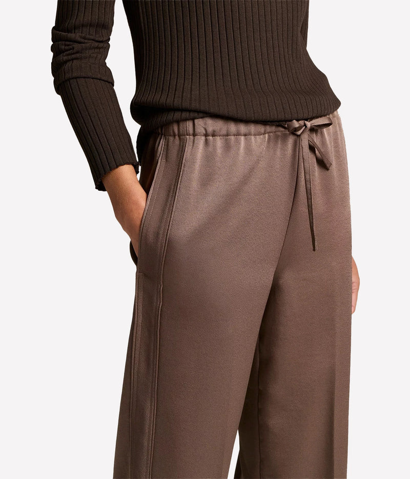 A close-up of a person wearing wide-leg taupe-brown drawstring sweatpants
