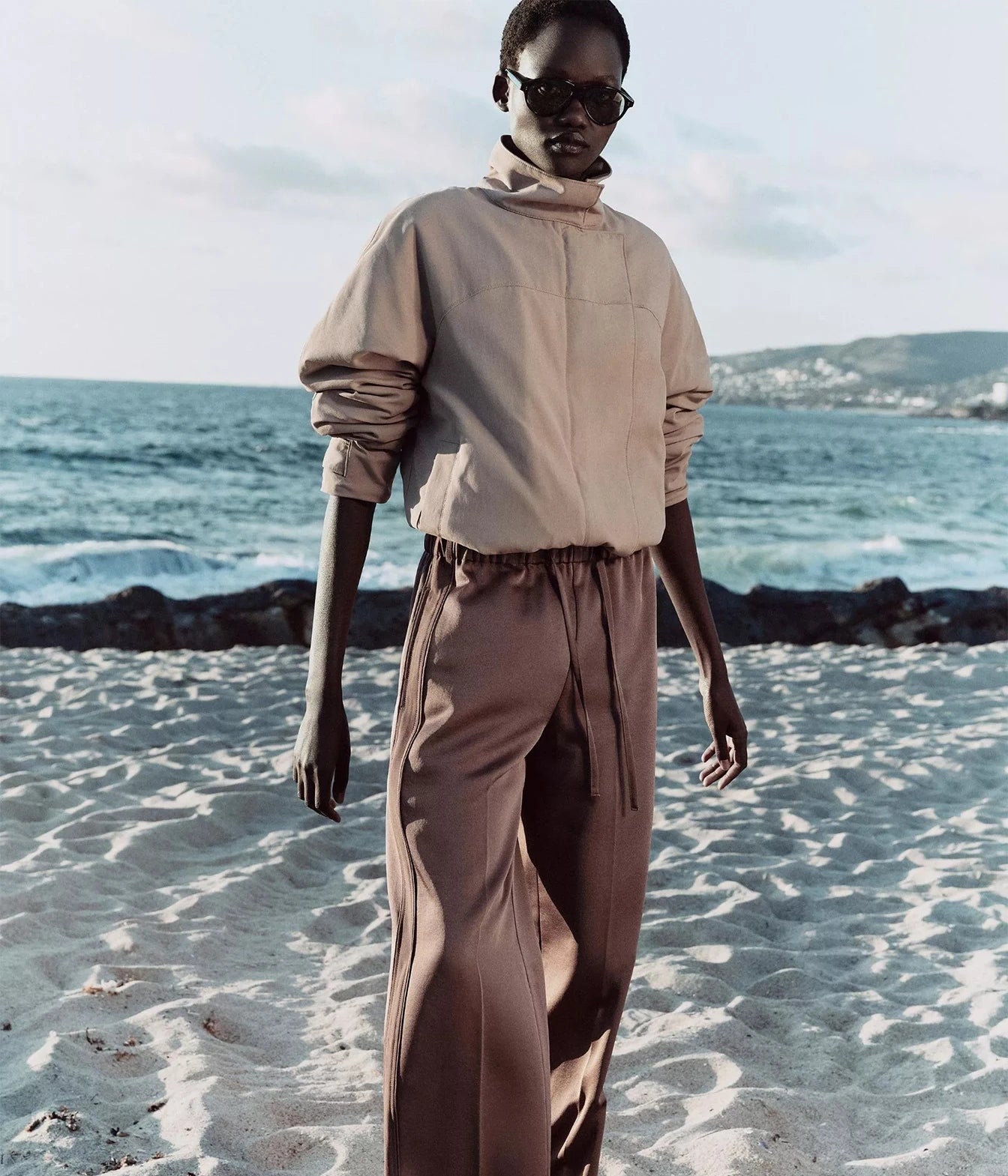 A model wearing a beige high-neck long-sleeve top and brown wide-leg trousers