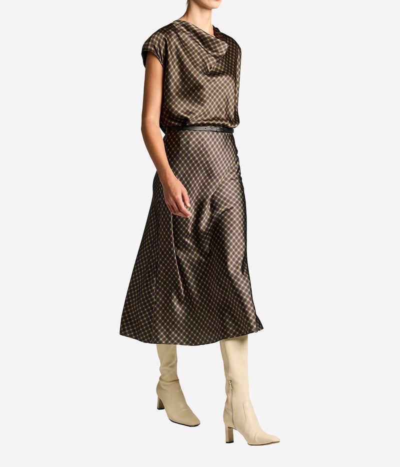 Side view of a model walking in the Vince Ombre Plaid Skirt In Black Camel with the matching blouse and cream boots, showing the skirt's fluid movement