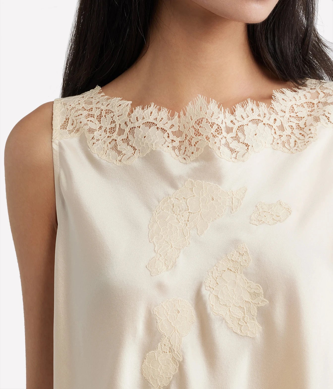 Close-up of a sleeveless cream satin top with floral lace trim at the neckline and matching lace appliques on the front, worn by a model.