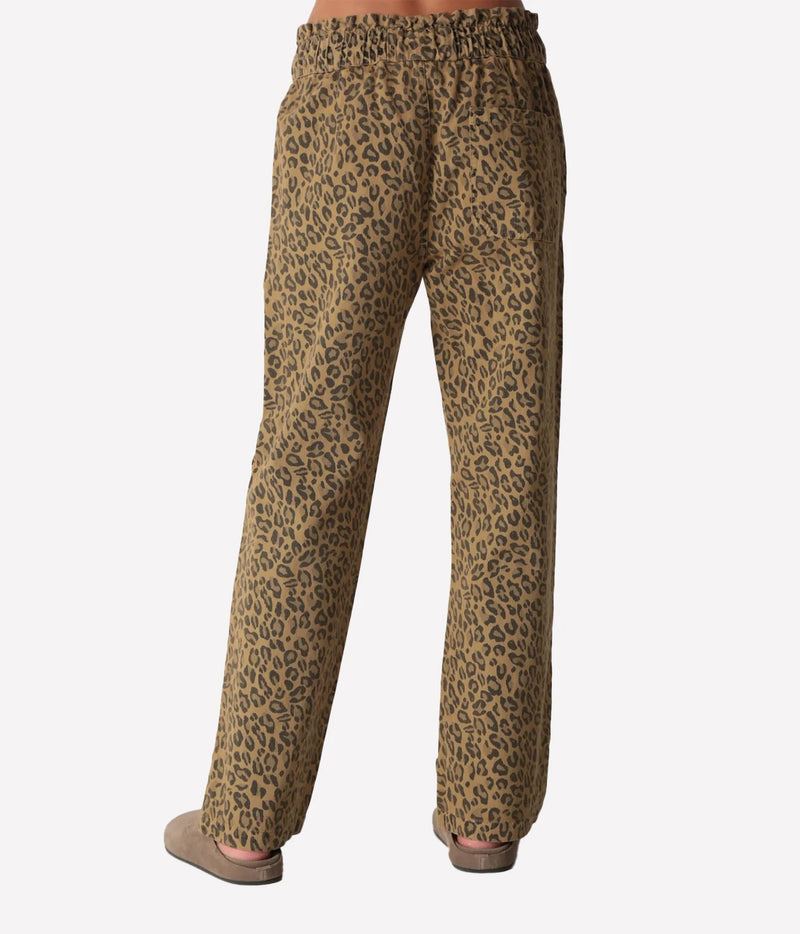 Back view of a model wearing the Electric Rose Easy Leopard Pant in Natural, showing the smocked elastic waistband and full-length straight leg, with taupe suede clogs