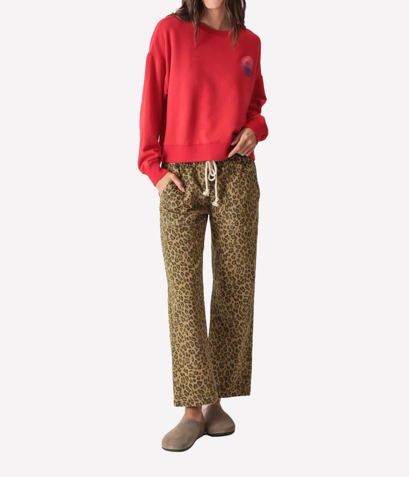 Full-length front view of a model wearing the Electric Rose Easy Leopard Pant in Natural with a red crew-neck sweatshirt, a hand in her pocket and taupe suede clogs