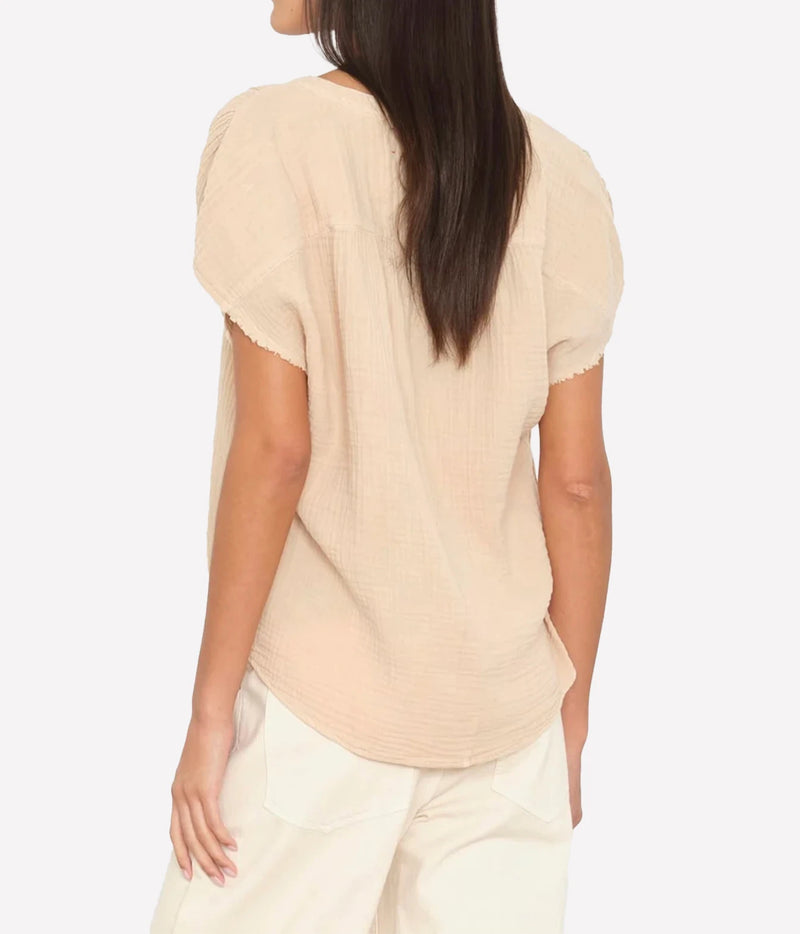 A woman shown from the back wearing a light beige short-sleeve textured top and cream pants.