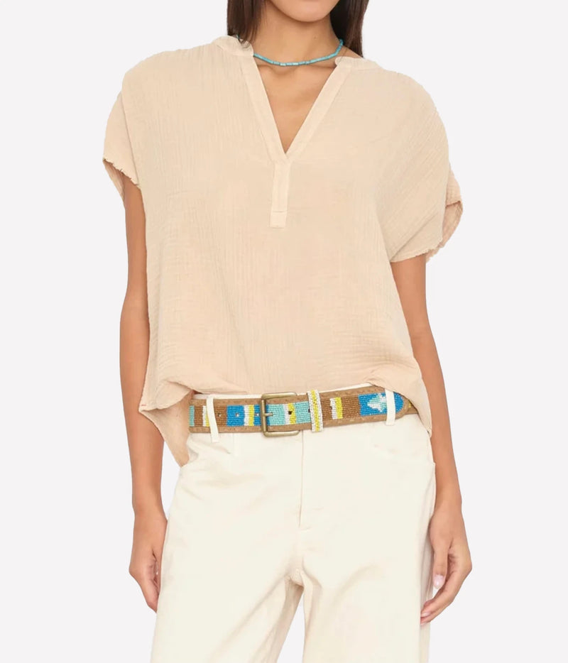A woman wearing a light beige short-sleeve V-neck top with a relaxed fit, paired with cream pants and a patterned belt.