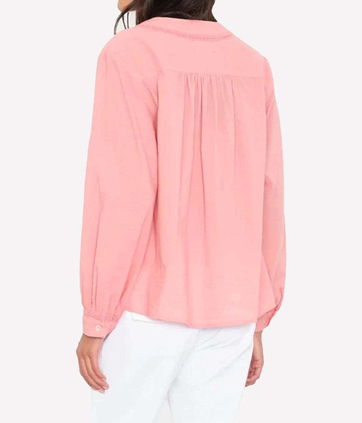 A woman shown from the back wearing a light pink long-sleeve blouse with gathered detailing at the back and white pants.