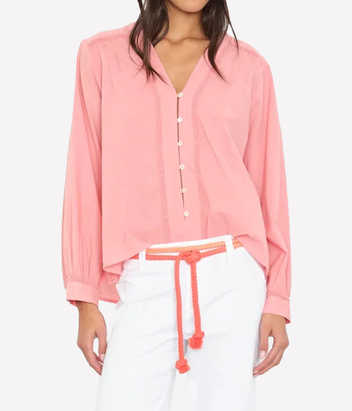 A woman wearing a light pink long-sleeve button-front blouse with white pants and a coral drawstring belt.