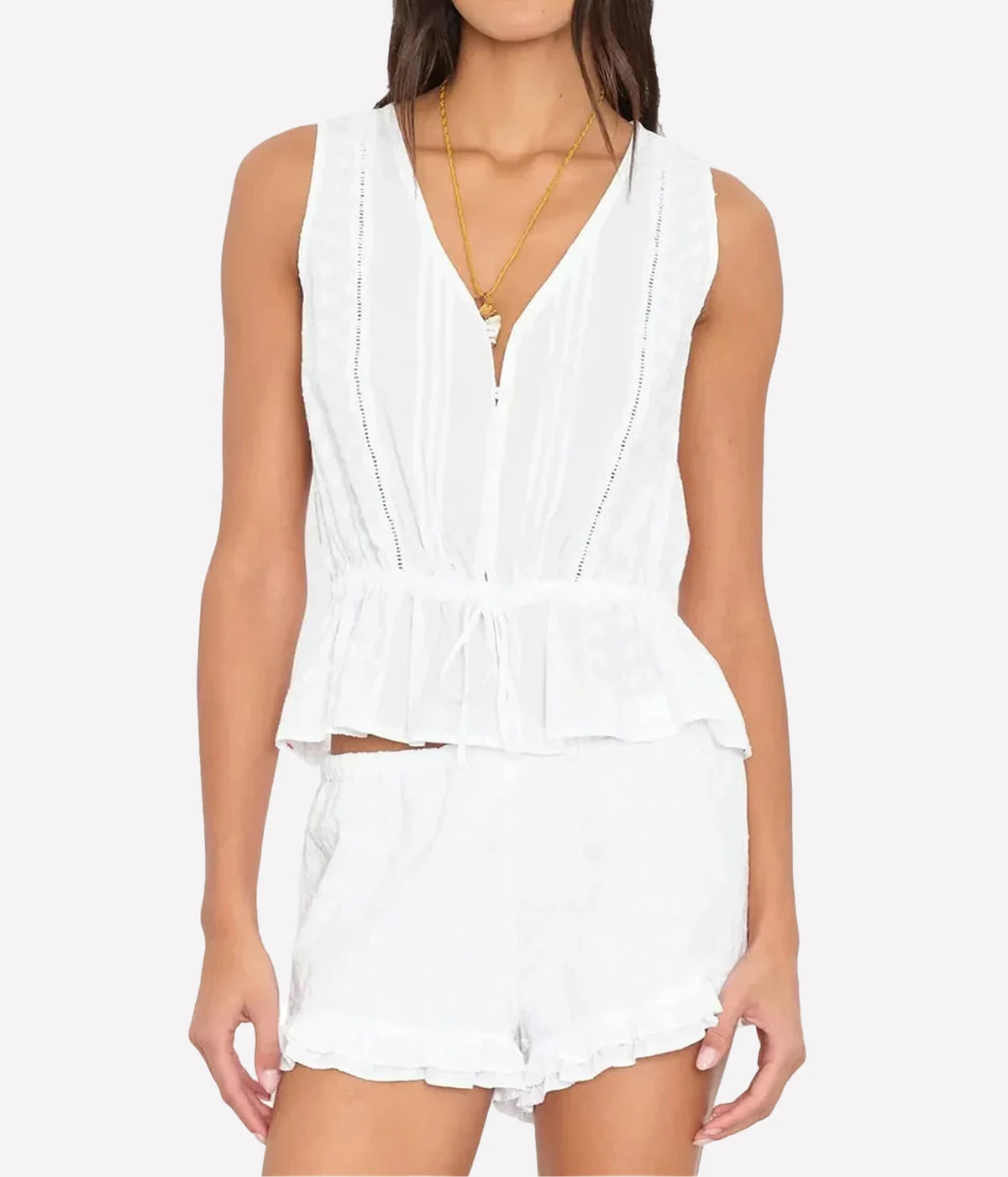 Model wearing the Xirena Emma Top in Blanc with the drawstring tied at the waist, styled with matching white ruffle-hem shorts and a layered gold pendant necklace