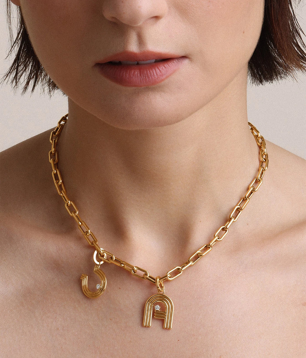 Model with a short bob wearing the Adina Reyter Groovy Diamond Horseshoe Hinged Charm in 14K Yellow Gold on a chunky gold link chain with another gold charm