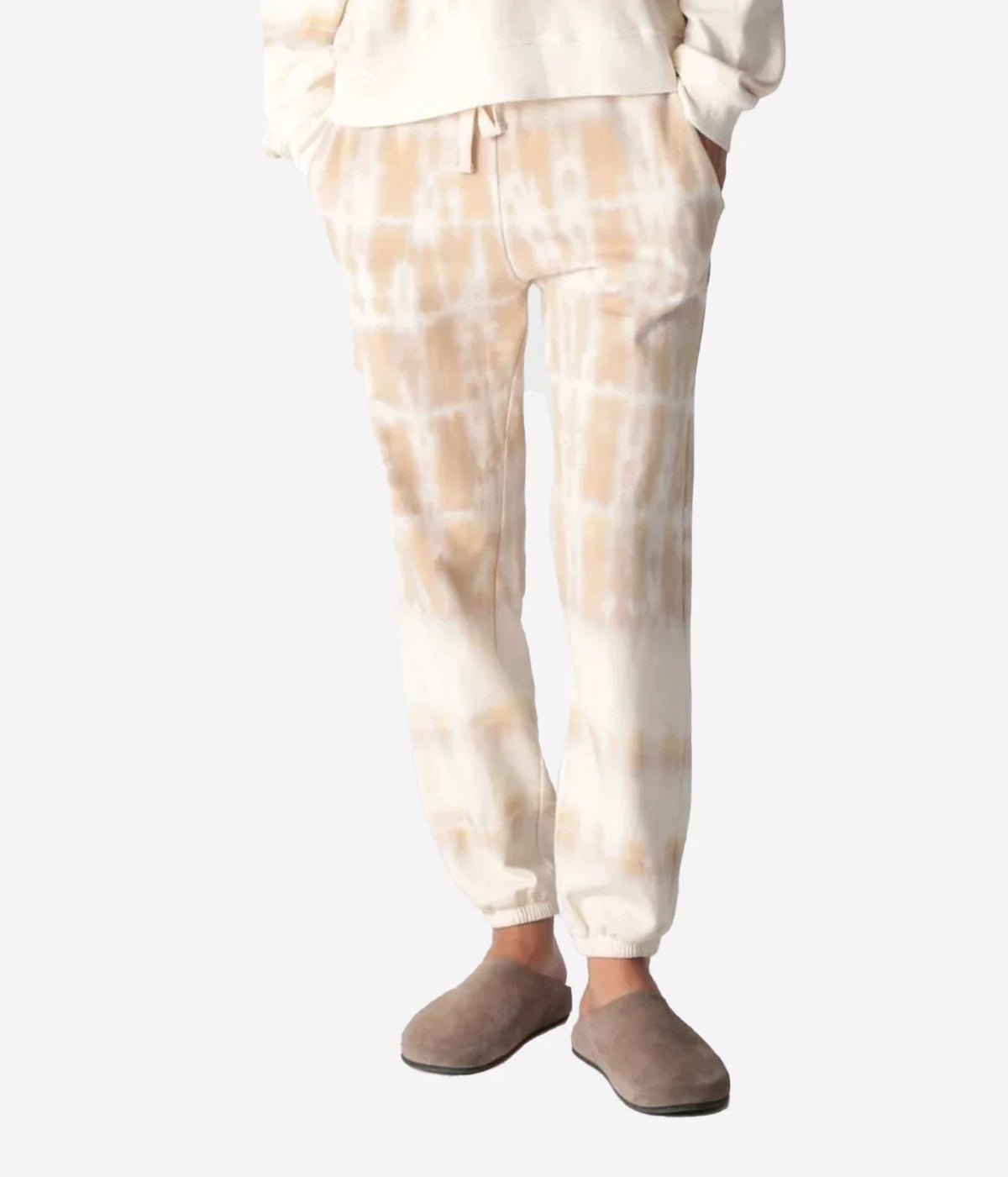 Front view of a model wearing the Electric Rose Classic Horizon Jogger in Dune Ivory, showing the drawstring waist, side pockets and cuffed ankles, with an ivory sweatshirt and taupe suede clogs